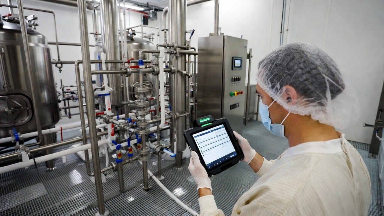 A food and beverage manufacturing plant floor with a worker using a mobile tablet to complete a digital inspection checklist