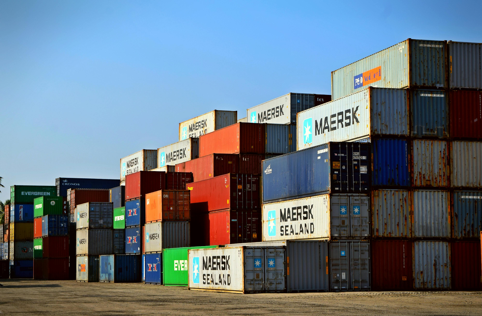 Colorful shipping containers stacked high at a port yard under a clear blue sky.