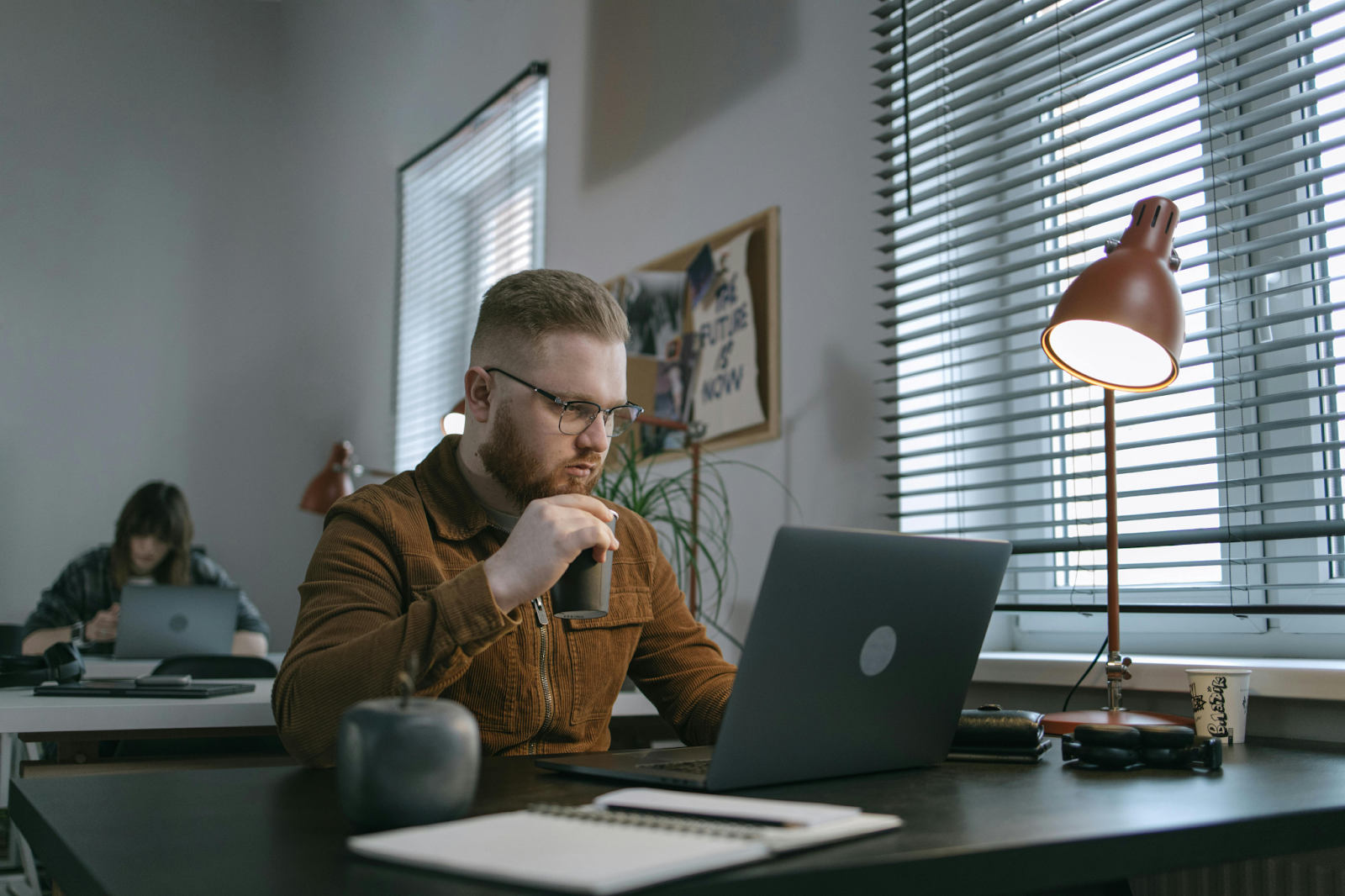 Man in glasses and brown corduroy jacket working on a laptop at an office desk