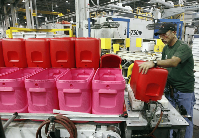 Factory worker handling red plastic containers on a production line in an industrial manufacturing facility.