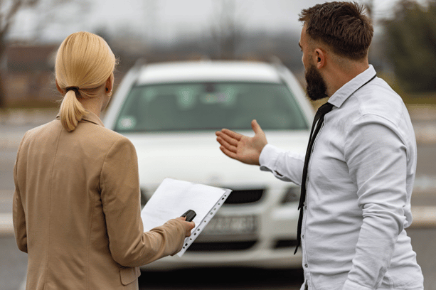 Man showing a white car to a woman holding a clipboard, likely during a car rental or sales inspection.